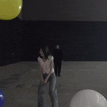 a woman in a white shirt and blue pants stands in front of two yellow balloons