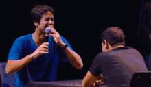 a man in a blue shirt is crying while talking into a microphone while another man looks on .