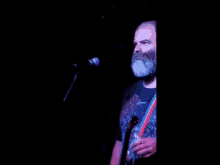 a man with a beard is singing into a microphone while holding a guitar
