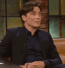 a man in a suit is sitting on a couch with his hands folded and a pen in his hand .