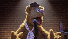 muppet fozzie bear singing into a microphone with a brick wall in the background