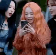 three women are standing next to each other and one of them is looking at her phone .