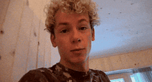 a young man with curly blonde hair is taking a selfie .