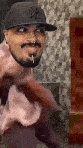 a man with a beard wearing a ny hat and a pink shirt