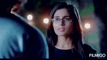 a woman wearing glasses is standing next to a man and looking at him .
