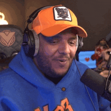 a man wearing headphones and an orange hat is sitting in front of a microphone and smiling .