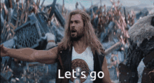 a man with long hair and a beard is standing in front of a crowd and says let 's go .