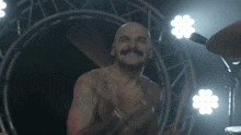 a shirtless man with a mustache is applauding in front of a drum set