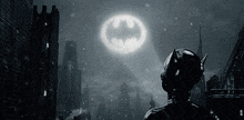 a man in a batman suit stands in front of a large batman logo