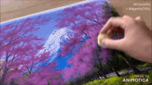 a person is painting a picture of a mountain with pink flowers