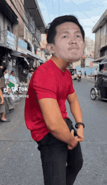 a man in a red shirt is standing in the middle of a street with a motorcycle in the background .