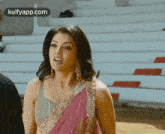 a woman in a pink saree is standing in front of a row of empty seats .