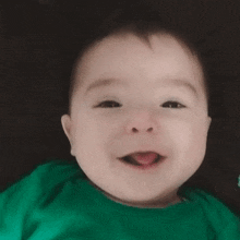 a baby in a green shirt is laying down on a bed .