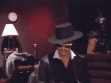 a man wearing a top hat and sunglasses stands in a room