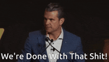 a man speaking into a microphone with the words we 're done with that shit behind him