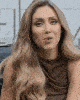 a woman with long blonde hair wearing a brown top