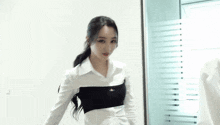 a woman in a white shirt is holding a bottle of water in front of a window
