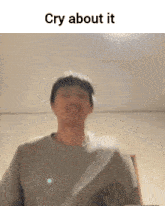 a man in a gray shirt is standing in front of a wall with the words cry about it above him .