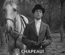 a man in a hat is standing next to a white horse .