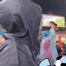 a man in a hooded jacket stands in front of a crowd of people at a soccer game