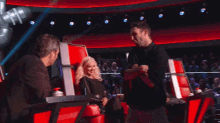 a man and a woman are sitting in red chairs on a stage talking to each other .