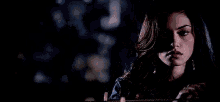 a woman is sitting in a dark room holding a rope and looking at the camera .