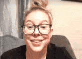 a woman wearing glasses and a bun is smiling and sitting in a chair .