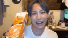 a man is holding a carton of orange juice in front of his face