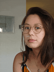 a woman wearing glasses and a necklace looks at the camera with her eyes closed