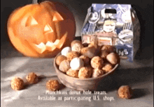 a bowl of donut hole treats next to a pumpkin with a face carved into it