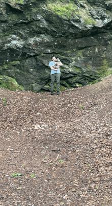 a man holds a baby in his arms in front of a rock wall