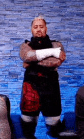 a man with a bandaged arm is standing in front of a brick wall with his arms crossed .