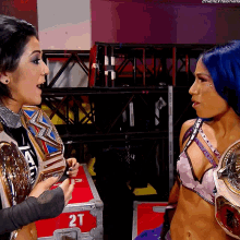 a woman with blue hair is talking to another woman in front of a 2t box