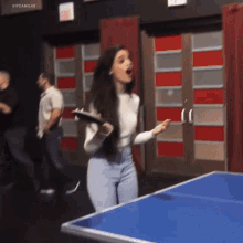 a woman is standing in front of a blue ping pong table with her mouth open