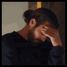 a man with a ponytail is covering his face with his hand .