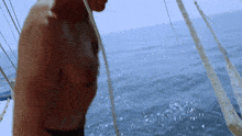 a shirtless man stands on a sailboat in the ocean