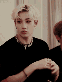 a man wearing a black shirt and a chain around his neck is looking at something