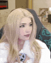 a woman with blonde hair and blue eyes is sitting in a chair and looking at the camera .