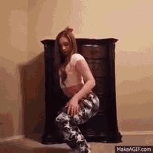 a woman in a crop top and leggings is squatting in front of a dresser .