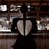 a woman in a black dress sits at a bar with a braided ponytail