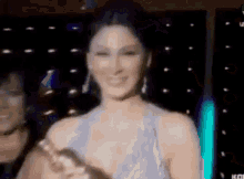 a woman in a blue dress is smiling while holding a trophy in a dark room .