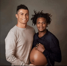 a man holding a pregnant woman 's belly smiles with another man