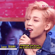 a young man is singing into a microphone while wearing a denim jacket and a ring on his finger .
