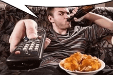 a man is sitting on a couch drinking beer and eating chips .