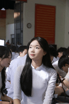 a girl with long black hair is sitting in a classroom with other students