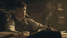 a man in a suit sits at a desk with a cigarette in his mouth