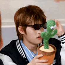 a man wearing sunglasses is holding a stuffed cactus in his hand .