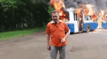 a man is standing in front of a burning bus on a road .