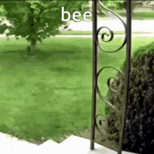a wrought iron gate is open to a lush green yard with the word bee written on it .