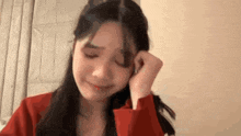 a young woman in a red jacket is crying and covering her face with her hands .